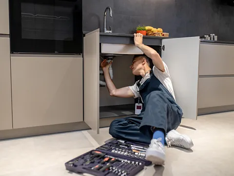 Rørlegger i arbeid under vask på moderne kjøkken